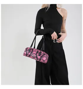 Detail of pink snakeskin cylinder bag with black handles held by model in black outfit