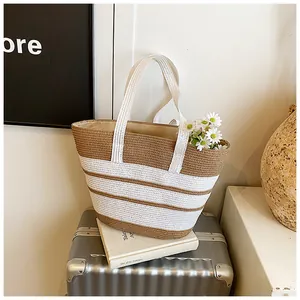 Dettaglio della borsa tote a righe in paglia intrecciata su una valigia estiva
