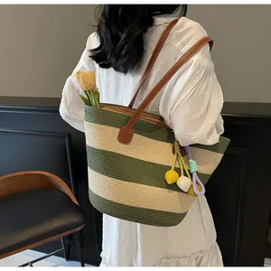 Detail of green striped woven tote bag with brown faux leather straps and pompom charm