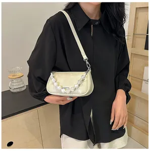 Dettaglio borsa beige effetto coccodrillo con manico di perle indossata da modella
