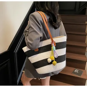 Close-up of striped woven tote bag featuring leather straps and colorful pompom charms