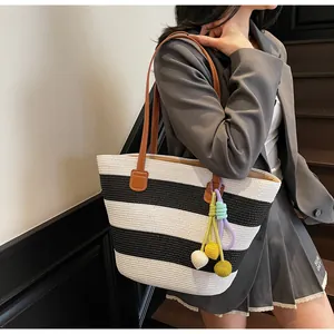Detail of woven black and white striped tote bag with colorful bag charm and leather strap
