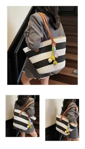 Close-up of black and white striped woven tote bag with brown leather straps and colorful charms