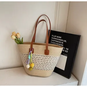 Detail of hand-woven straw tote bag with beige-white stitching and brown leather handle