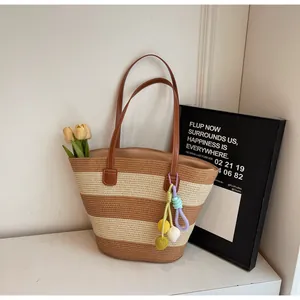 Close-up of striped woven tote bag with leather straps and a colorful fringe charm