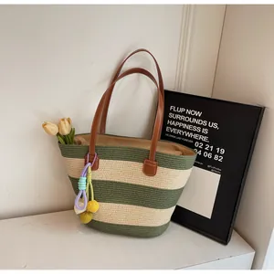 Close-up of green and cream woven tote bag with brown leather handles and colorful charms