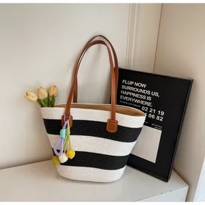 Close-up of woven tote bag with black and white stripes and colorful pompom charms