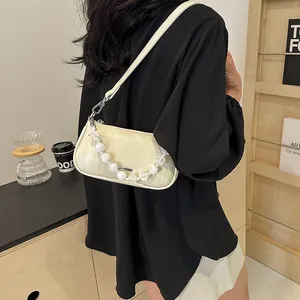 Borsa a tracolla crema minimalista con catena di perle indossata da modella in interni