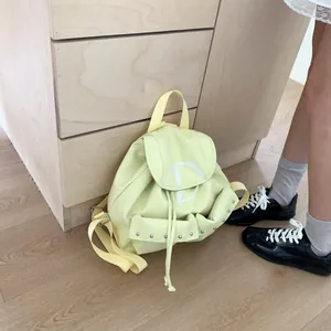 Detail of light yellow nylon backpack showing drawstring closure and metal rivet accents