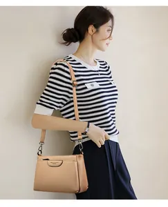 Close-up of beige leather crossbody bag with adjustable strap and grain texture on model