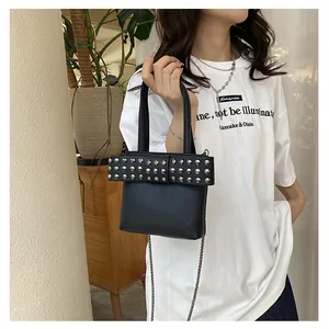 Détail d'un sac en cuir noir avec rivets argentés et bandoulière chaîne porté par un mannequin