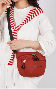 Detail view of brick red nylon crossbody bag with dual zippers and adjustable strap