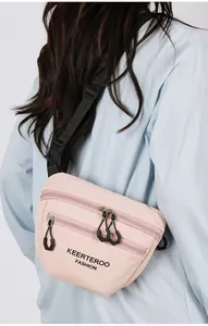 Rear view of a light pink nylon crossbody bag with double zippers and black strap
