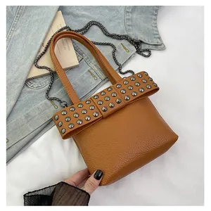 Détail d'un sac à main en cuir grainé marron avec nœud riveté et bandoulière chaîne
