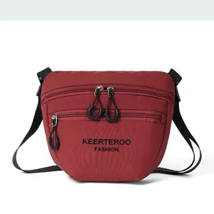 Detail view of burgundy nylon crossbody bag featuring triple zipper pockets and black strap