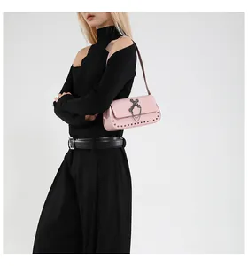 Detail of pink rivet shoulder bag with metal cross and chain on model in black knit