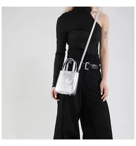 Detail of silver metallic handbag with heart charm and delicate chain strap on model
