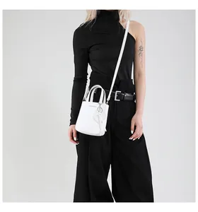 Chic white mini bucket bag with heart pendant shown on model in stylish black outfit
