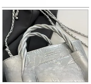 Close-up of silver textured handbag with braided handle and chain strap detail