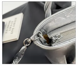 Detail of silver metallic textured bucket bag with zipper and woven chain strap