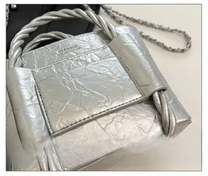 Detail of silver bucket bag with pleated texture and dual-strand braided handle