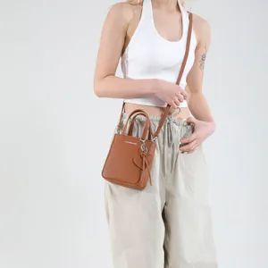 Brown bucket bag with top handle and heart charm shown on model in minimal studio setting
