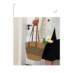 Detail of a large woven tote bag featuring beige straw texture and brown leather handles