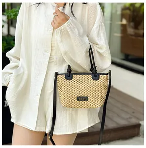 Detail of woven straw bucket bag with black leather trim and metal branding plaque