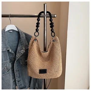 Close-up of woven shoulder bag featuring black beaded handles and logo patch detail