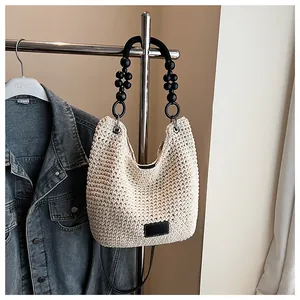 Detail of beige woven hobo bag featuring black beaded handle and leather logo patch