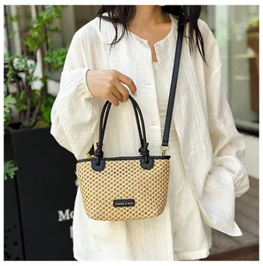 Detail of hand-woven straw bucket bag with black leather handles and adjustable strap