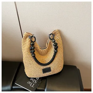 Detail of woven straw shoulder bag with beaded rope handle and logo patch on front