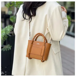 Detail of caramel mini bucket bag with twisted handle and metal chain on a model