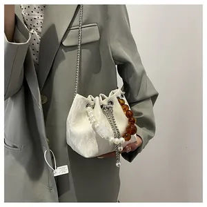 Detalle de bolso tipo saco blanco con asa de perlas y cadena de resina en color ámbar