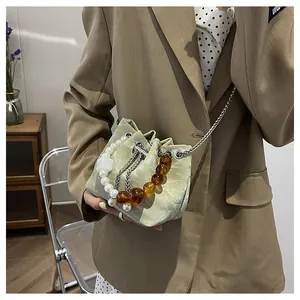 Detalle del bolso tipo saco verde claro con textura fruncida, asa de perlas y cadena metálica