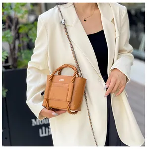 Detail of a brown bucket bag featuring a twisted woven handle and gold chain strap