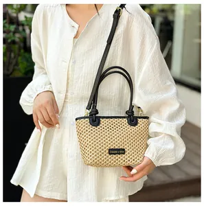 Detailed view of beige straw bucket bag with black leather handles and crossbody strap