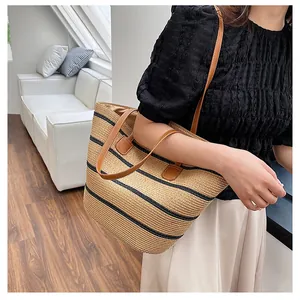 Close-up of woven straw tote bag featuring black stripes and brown leather straps