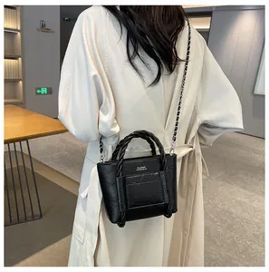 Detail of black leather bucket bag with woven handle and classic metal chain strap
