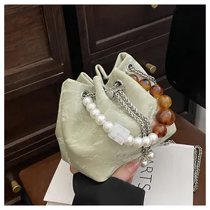 Detalle de bolso saco verde claro con perlas, toques ámbar y correa de cadena plateada