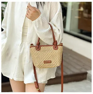 Detail of woven straw bucket bag with brown leather trim and adjustable shoulder strap