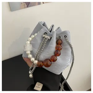 Detalle del bolso tipo cubo de terciopelo gris con perlas grandes y asa de ámbar con cadena