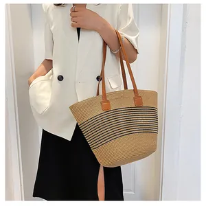 Detail of hand-woven straw tote bag featuring black stripes and faux leather straps