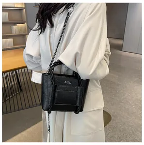 Detail of black textured bucket bag showing metal chain and braided handle on model