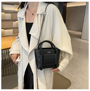 Chic black tote bag with braided handles and chain strap shown with a trench coat