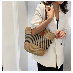 Detail of handwoven straw tote bag with black stripes and brown leather shoulder straps