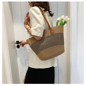 Detail of hand-woven straw tote bag with black stripes and brown leather shoulder straps