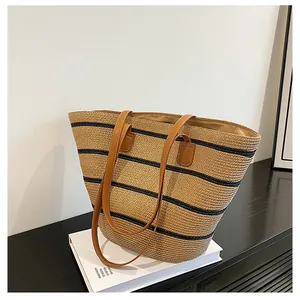 Detail of woven straw tote bag with black horizontal stripes and brown leather handles