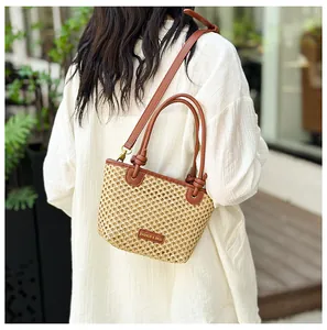 Detail of straw woven bucket bag with leather handles shown in a lifestyle outdoor setting