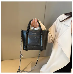 Detail of black textured bucket bag with woven handle and chain strap on a model